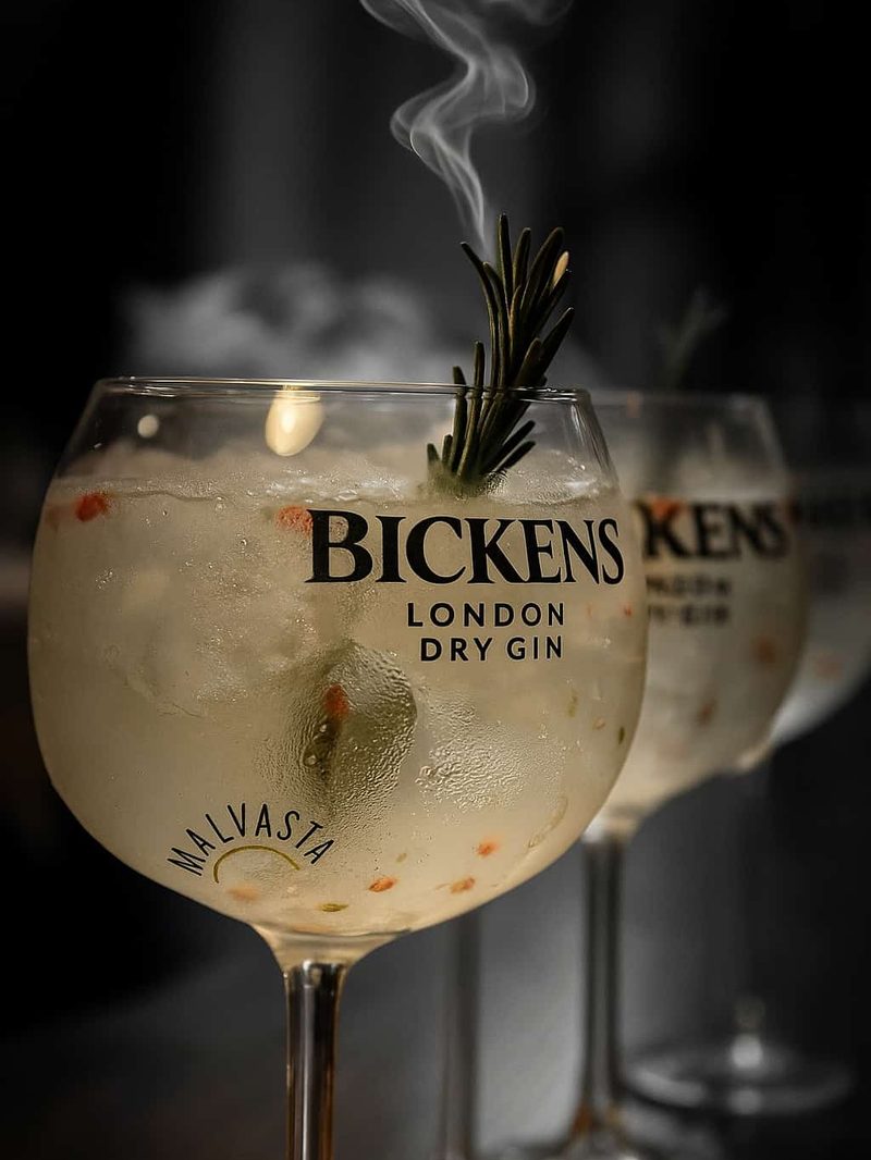 Gin tonic servito in un calice a palloncino con rosmarino, in un bicchiere inciso con il nome del locale.
