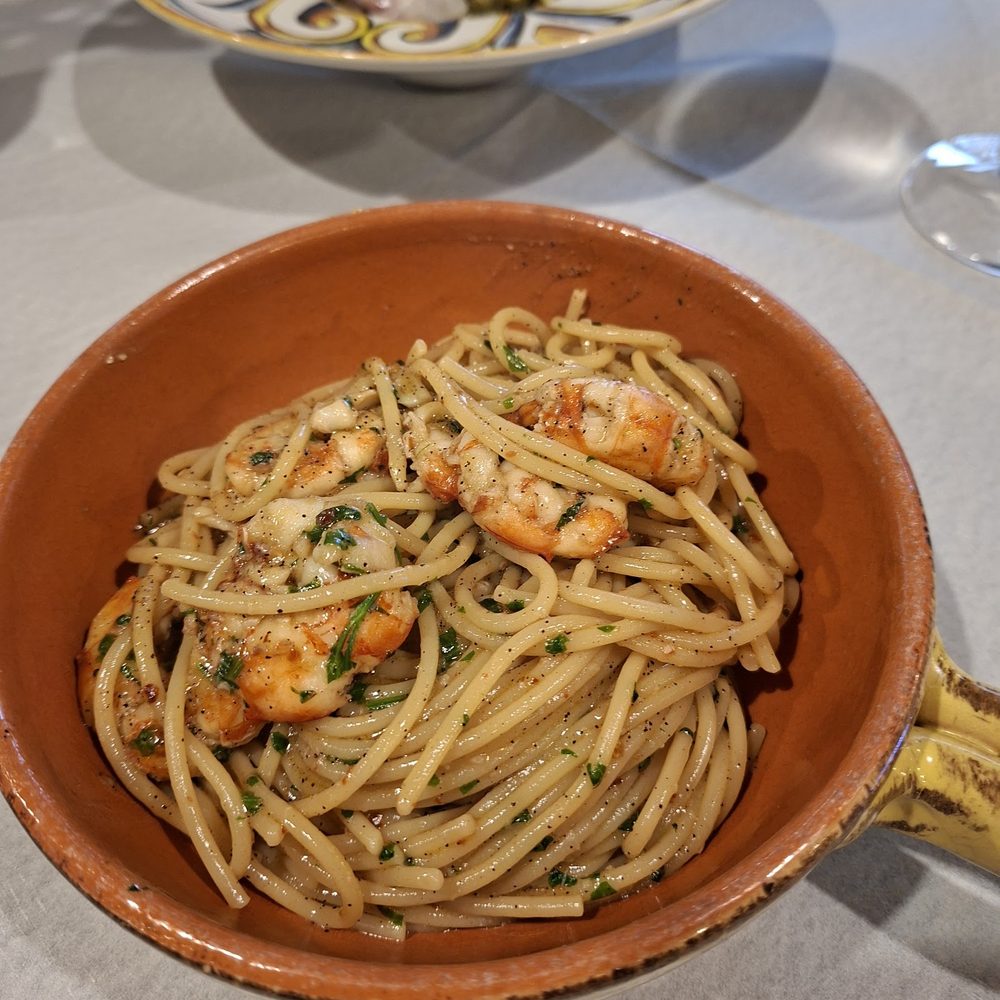 Spaghetto aglio, olio e peperoncino con gamberi rosa e prezzemolo, servito in una padella di terracotta.