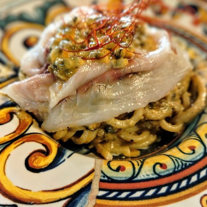 Tagliolino con crudo di orata e passion fruit, servito su un piatto siciliano dipinto a mano.