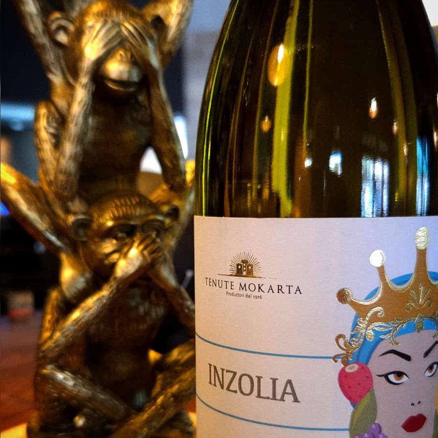Bottiglia di Inzolia IGP Terre Siciliane appoggiata sul bancone di legno del ristorante.